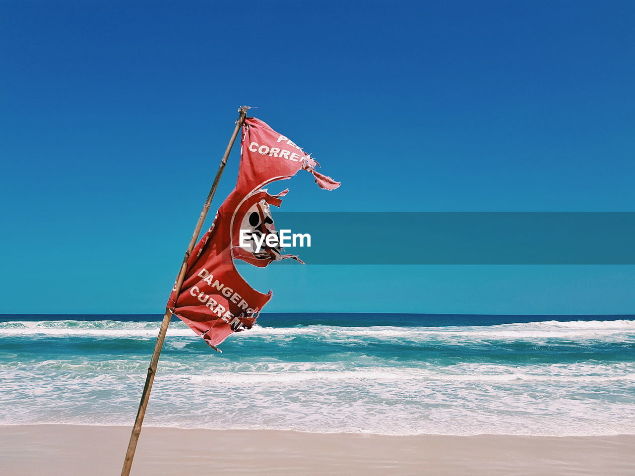 Torn flag at beach against clear blue sky
