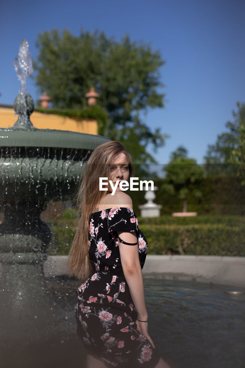 Portrait of young woman standing by fountain