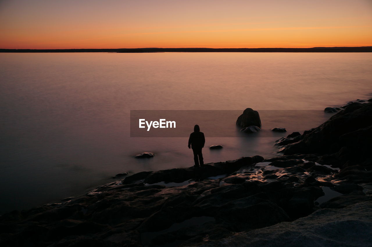 Rear view of man walking on beach against sky during sunset