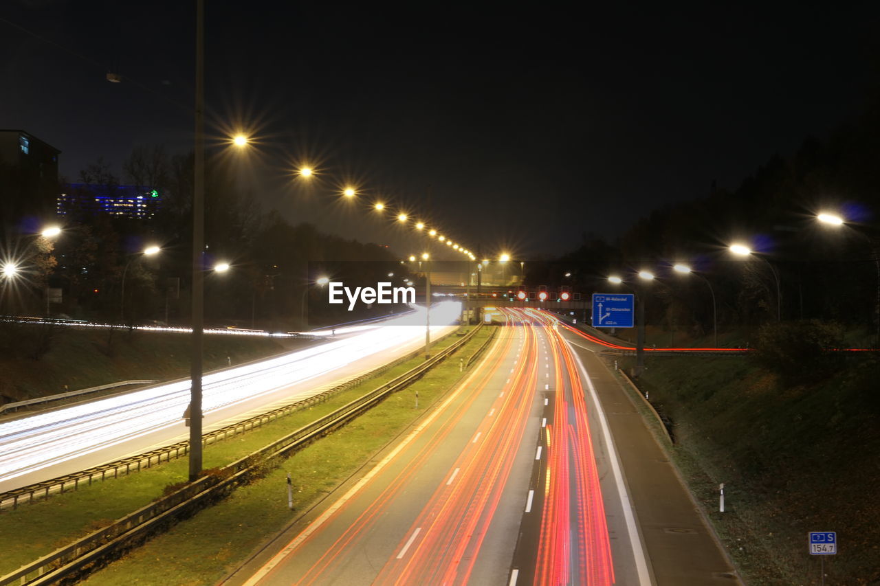 LIGHT TRAILS ON HIGHWAY IN CITY AT NIGHT
