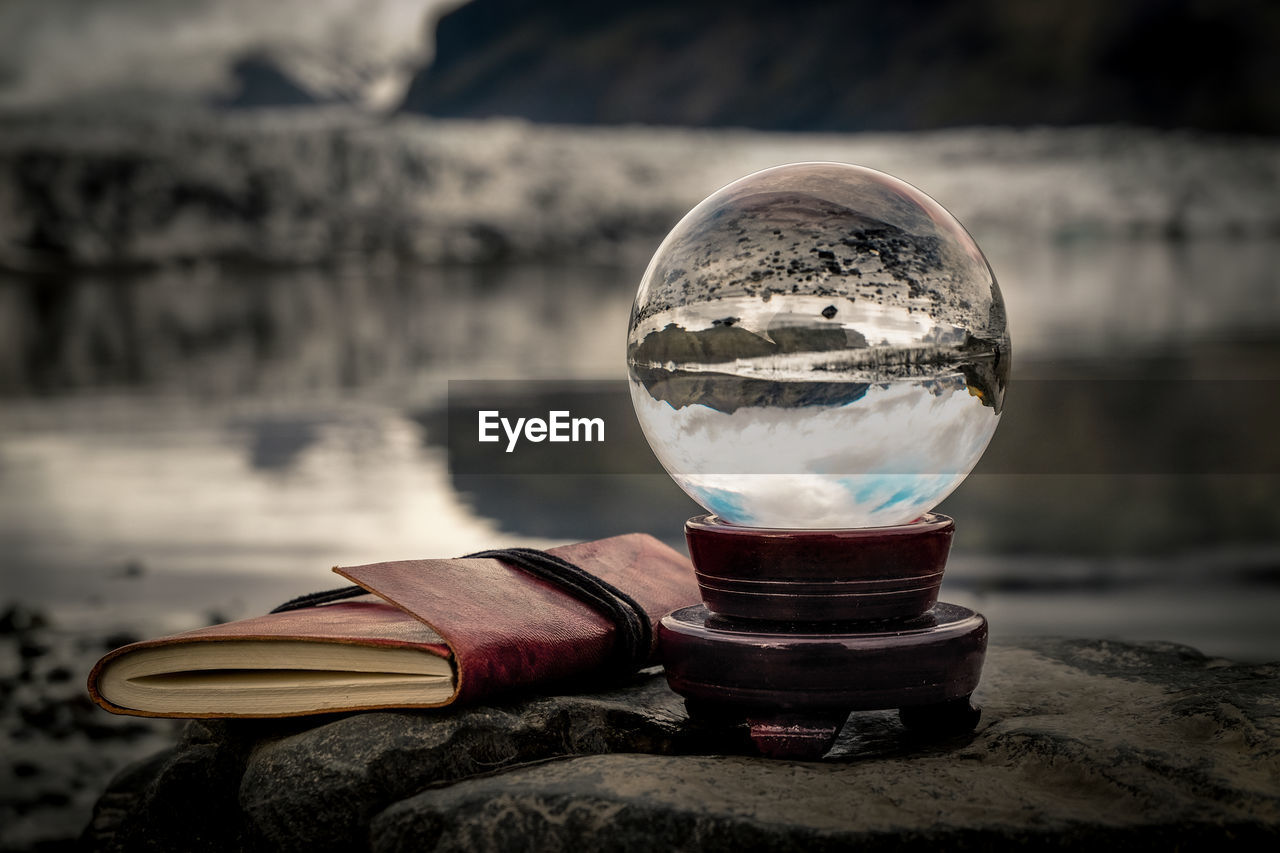 Close-up of crystal ball with reflection by book on rock