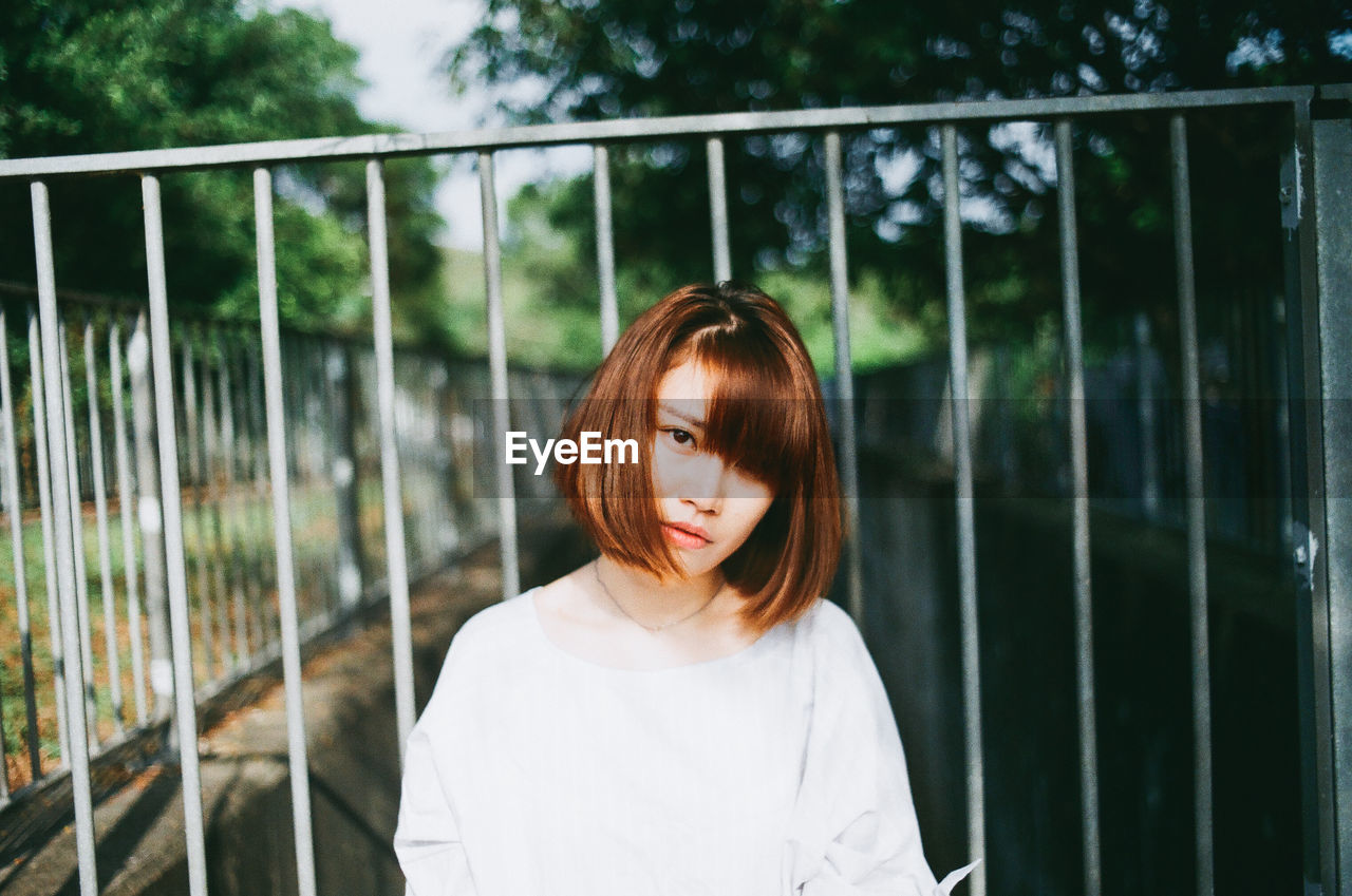 Portrait of woman standing against railing in park