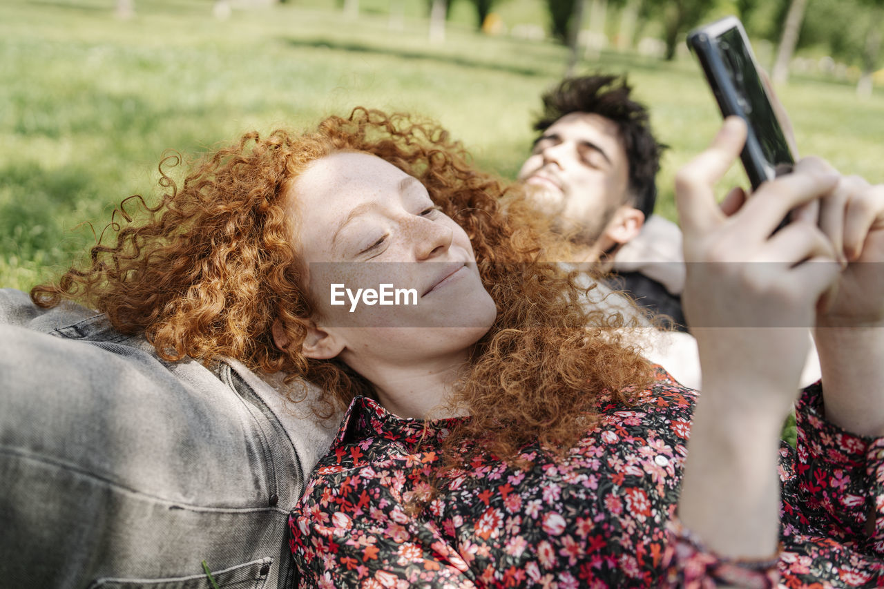 Smiling woman using smart phone while lying on boyfriend in park