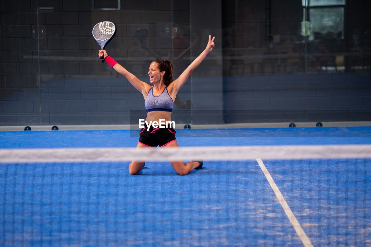 Portrait of beautiful young wimmer girl exulting on indoor padel tennis court