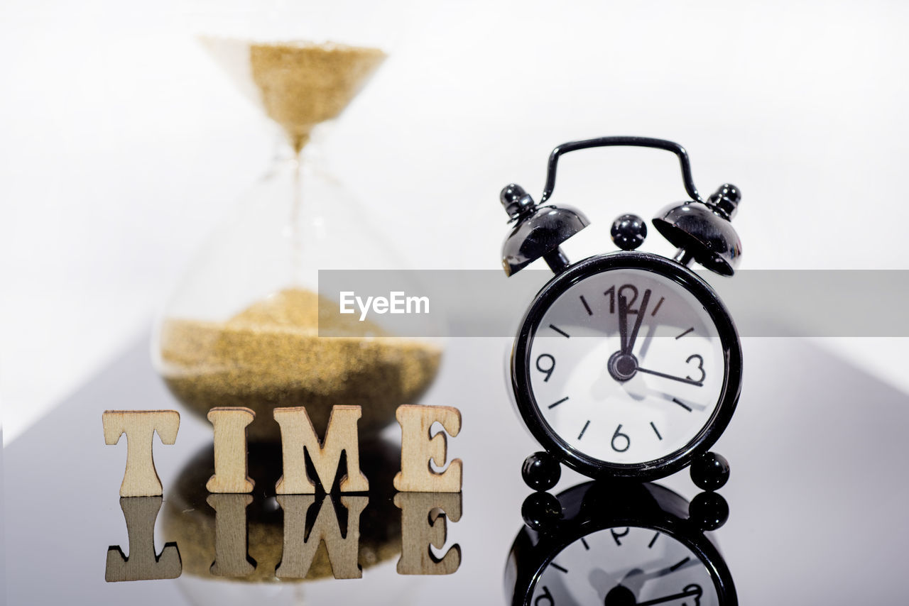 CLOSE-UP OF CLOCK ON GLASS TABLE AGAINST WHITE BACKGROUND