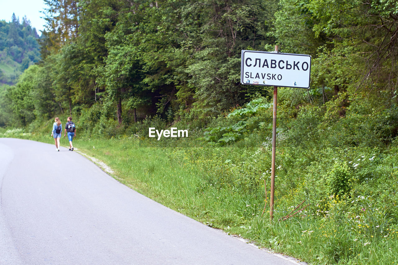 road, sign, plant, transportation, communication, lane, road sign, tree, text, trail, nature, day, western script, information sign, green, symbol, mountain pass, guidance, the way forward, men, infrastructure, full length, arrow symbol, lifestyles, travel, highway, growth, sports, outdoors, directional sign, leisure activity, asphalt, bicycle, warning sign, adult, beauty in nature, grass, mountain, non-urban scene, sky