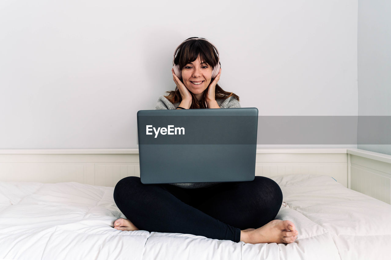 Young woman using laptop while sitting on bed at home