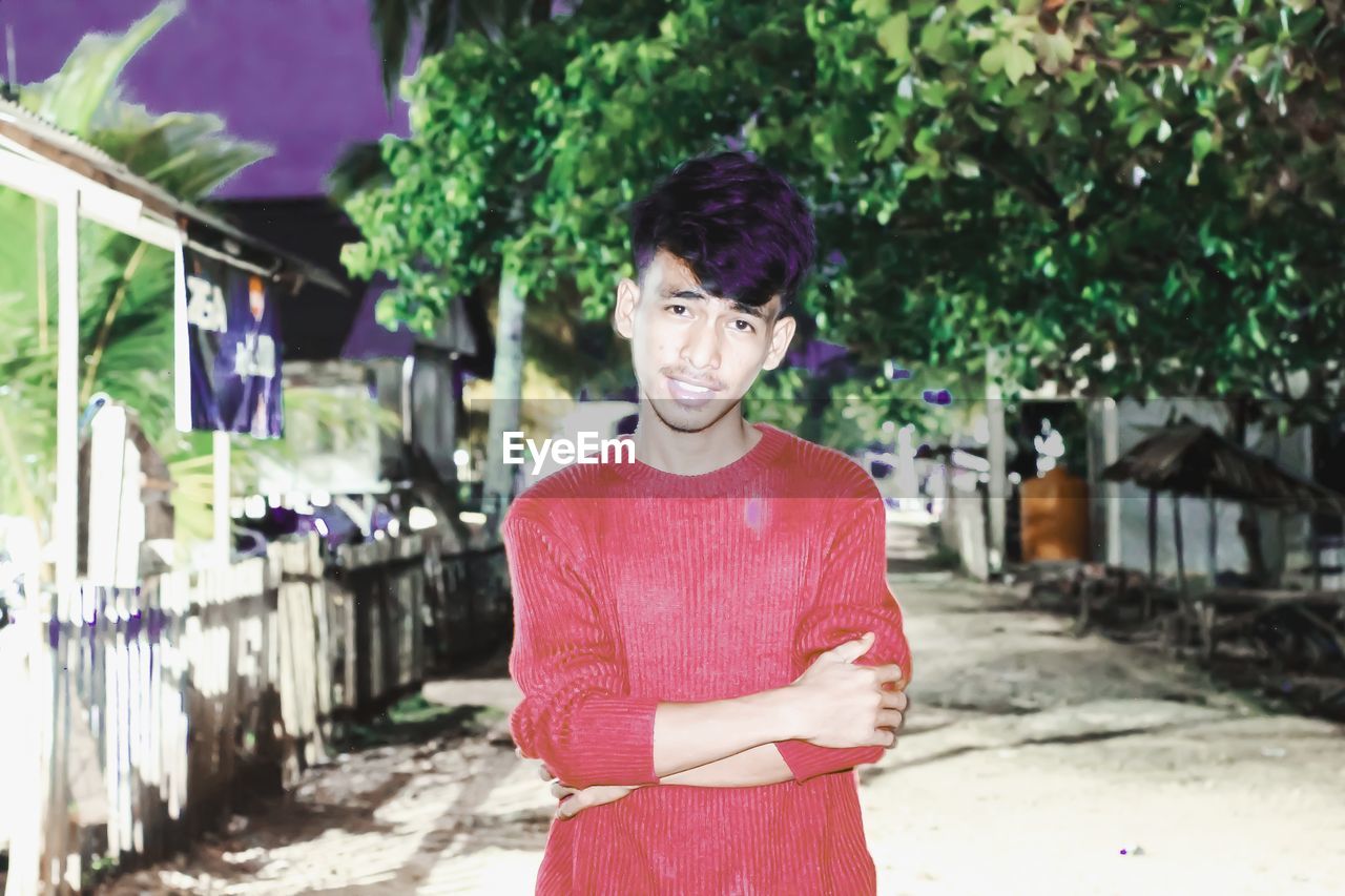 PORTRAIT OF YOUNG MAN STANDING AGAINST PURPLE PLANTS