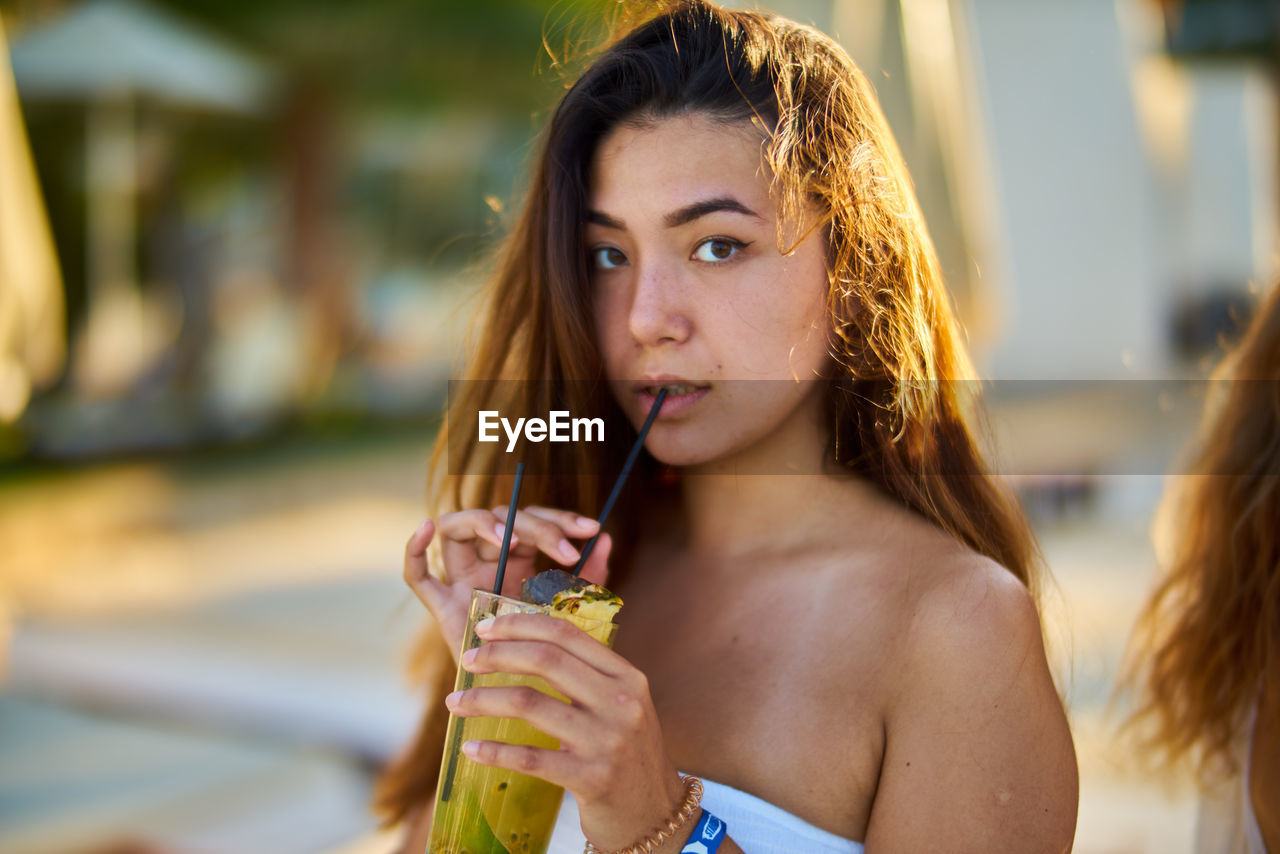 Portrait of young woman drinking juice from straw in city