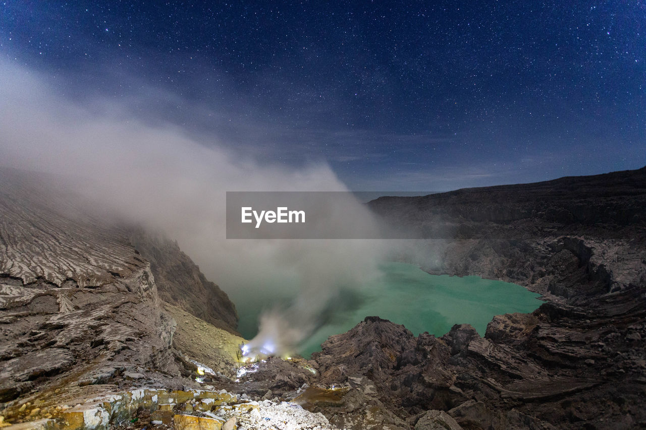 Smoke emitting from volcanic mountain against sky at night