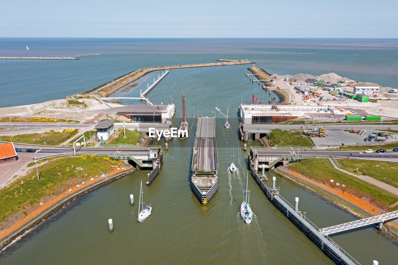 water, transportation, aerial photography, sea, high angle view, architecture, marina, mode of transportation, aerial view, built structure, dock, port, nature, coast, infrastructure, travel, day, city, nautical vessel, building exterior, travel destinations, horizon over water, road, beach, land, horizon, outdoors, sky, bird's-eye view, no people, waterway, vehicle, tourism, building, scenics - nature, business, environment, bay, channel, sunny, motor vehicle, bridge, industry, ship, car