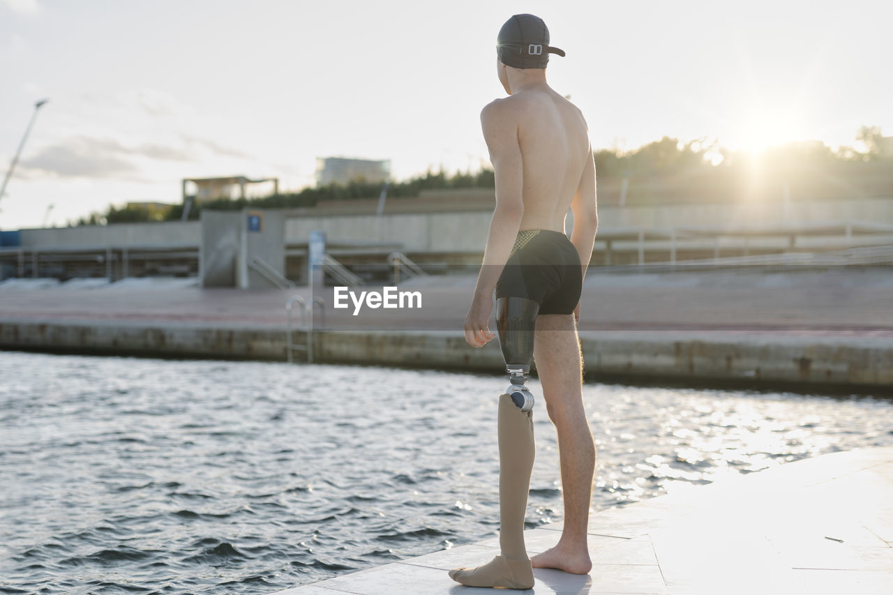 Young man looking at sea while standing on promenade during sunny day