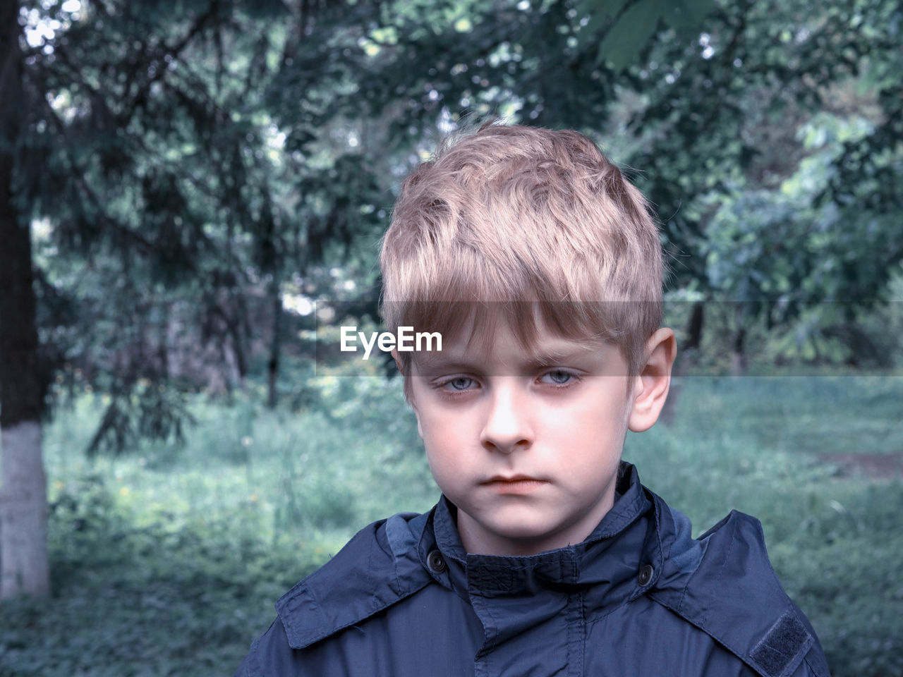 Close-up portrait of serious boy wearing raincoat in forest
