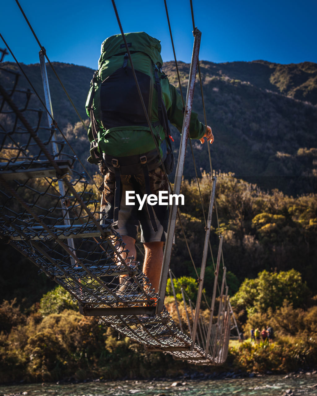 REAR VIEW OF MAN STANDING BY PLANTS AGAINST MOUNTAINS