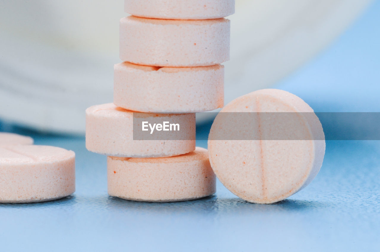 Pink tablet of medicine against light blue background, studio shot