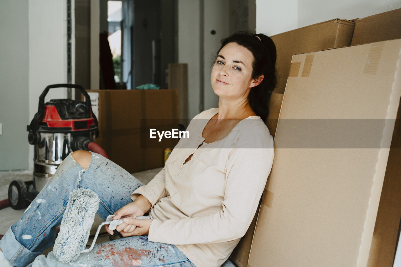 Portrait of smiling woman sitting by cardboard during home renovation