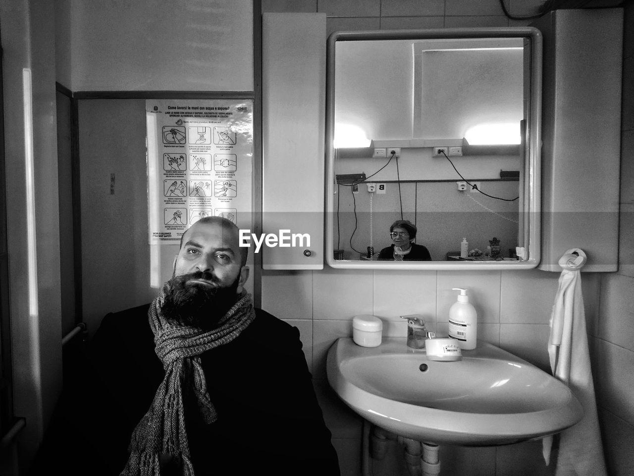 Matured man sitting in bathroom while woman reflecting in mirror