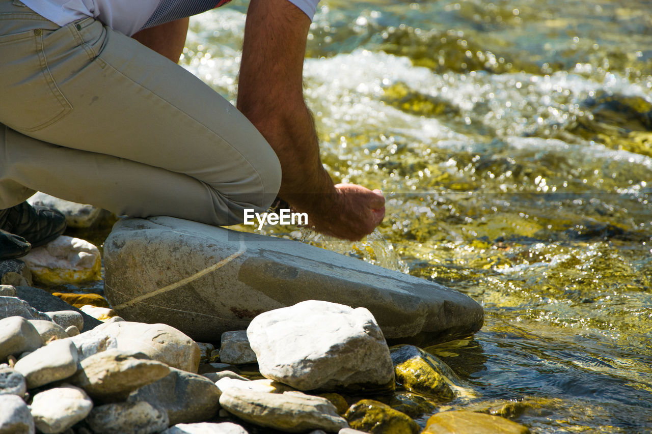 Low section of man with hands cupped by river 