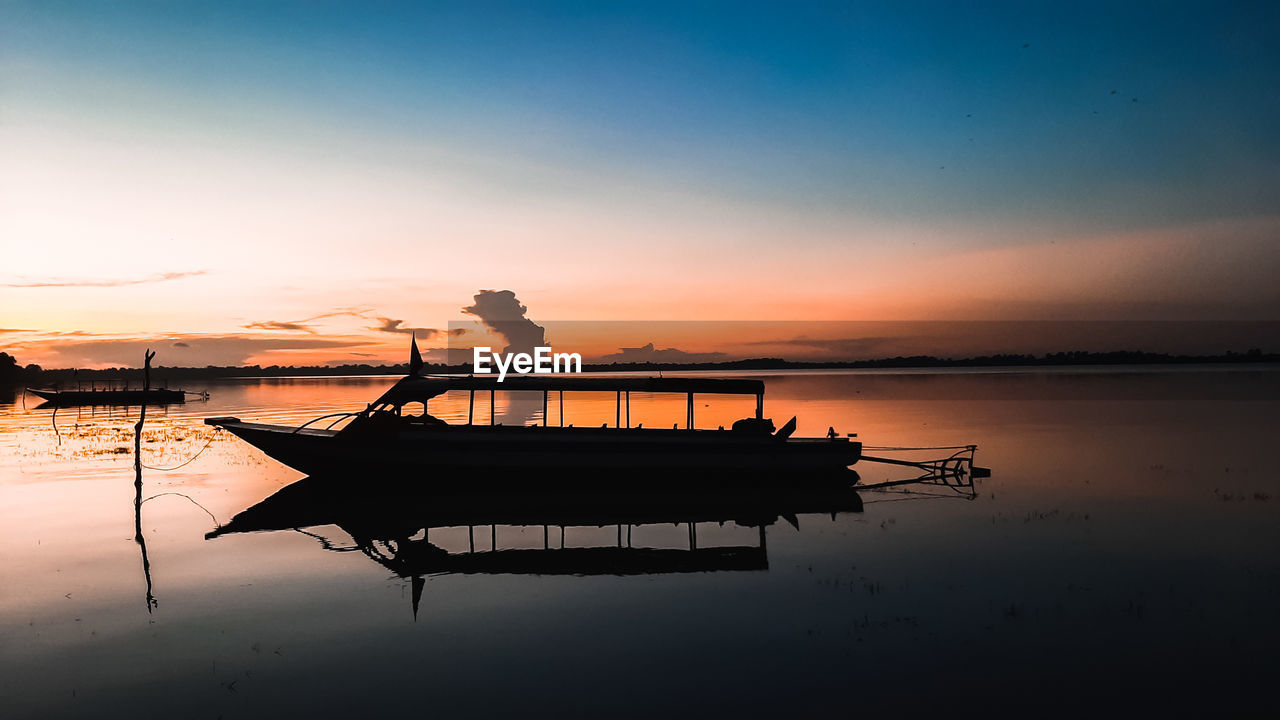 SILHOUETTE BOAT IN LAKE AGAINST SKY AT SUNSET