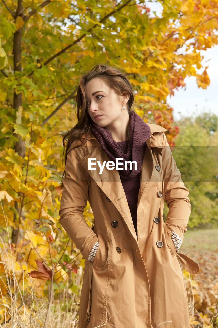 Woman wearing coat standing against trees in park during autumn