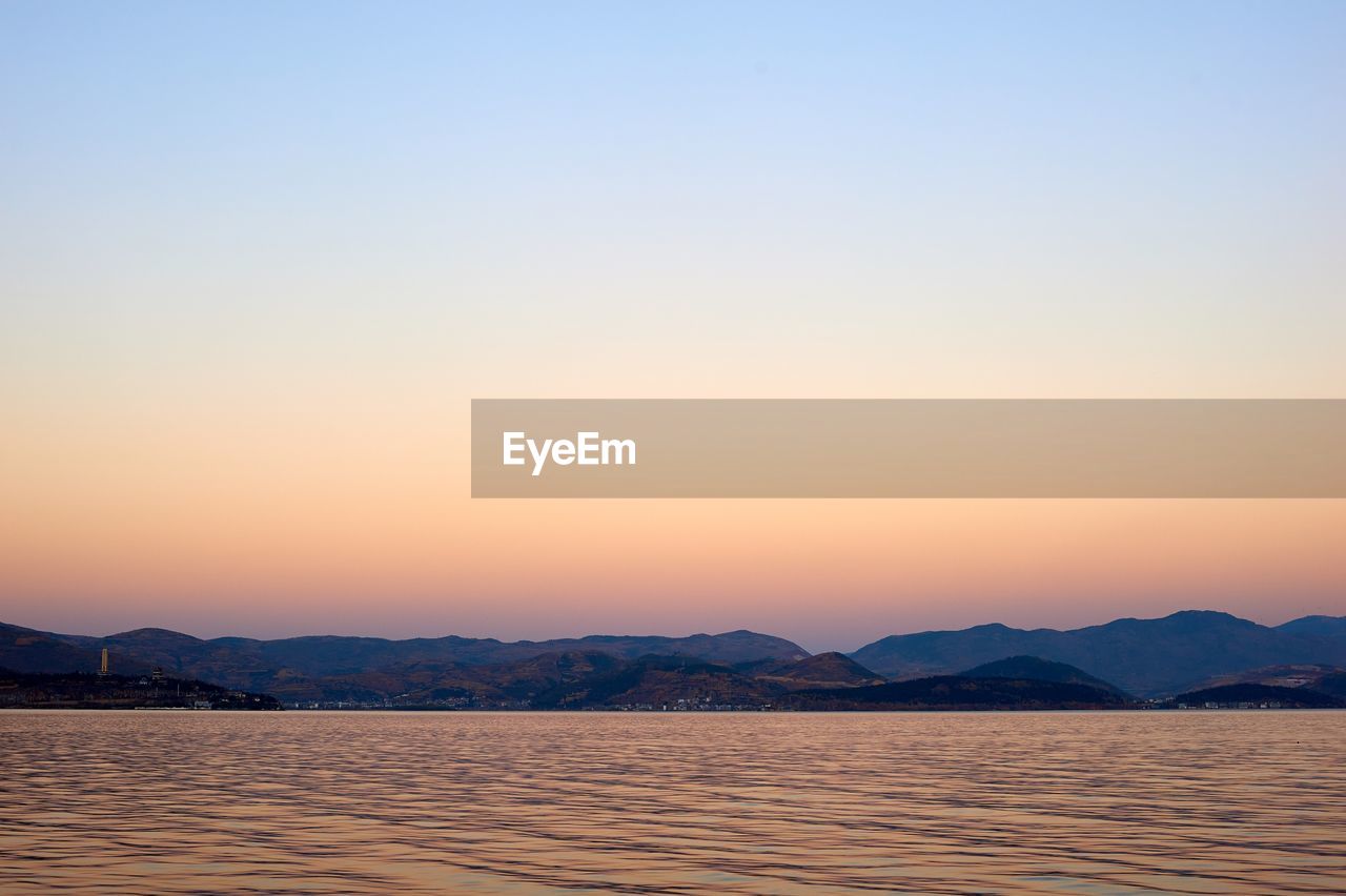 Scenic view of lake by mountains against clear sky during sunset