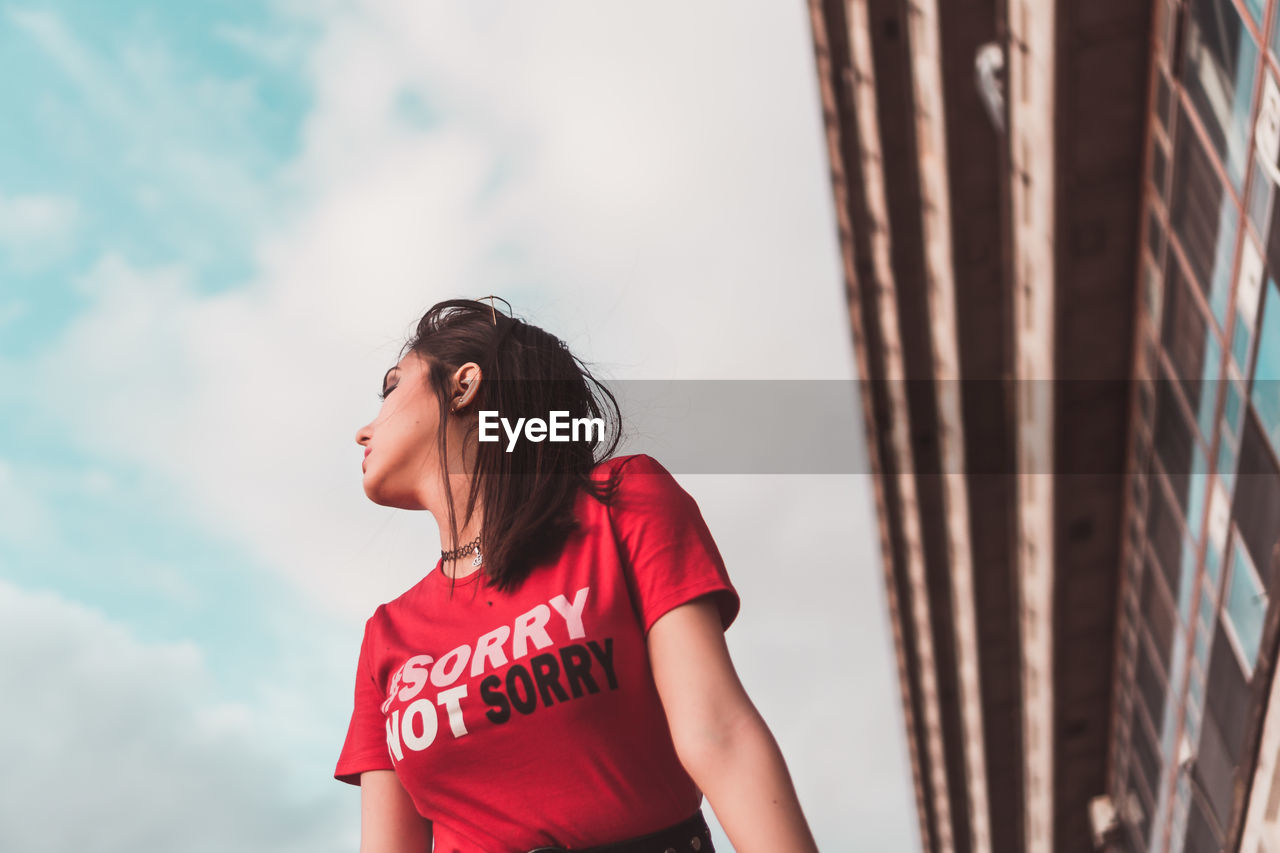 YOUNG WOMAN LOOKING AWAY AGAINST SKY