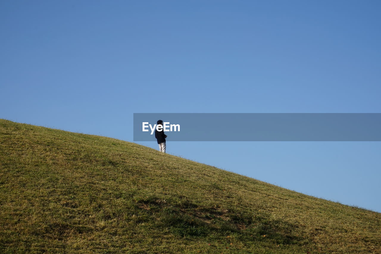 MAN WALKING ON DIRT ROAD AGAINST BLUE SKY