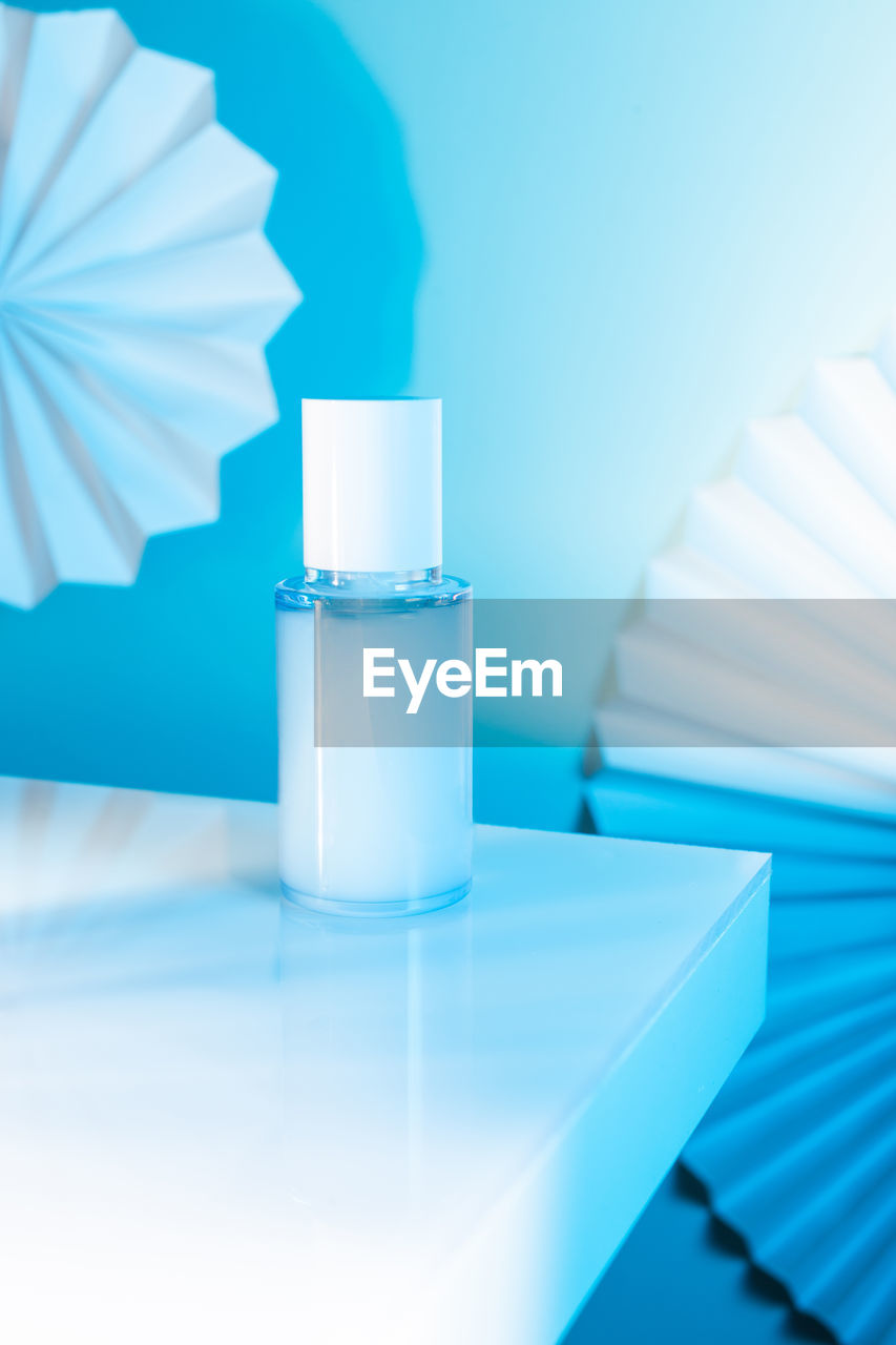 Cosmetic serum bottle on a white table, blue neon light, mock up
