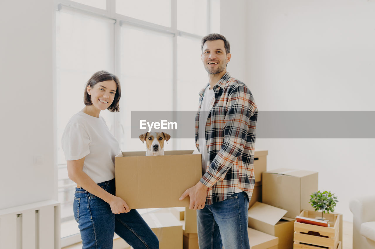 Portrait of smiling couple carrying puppy in box at home