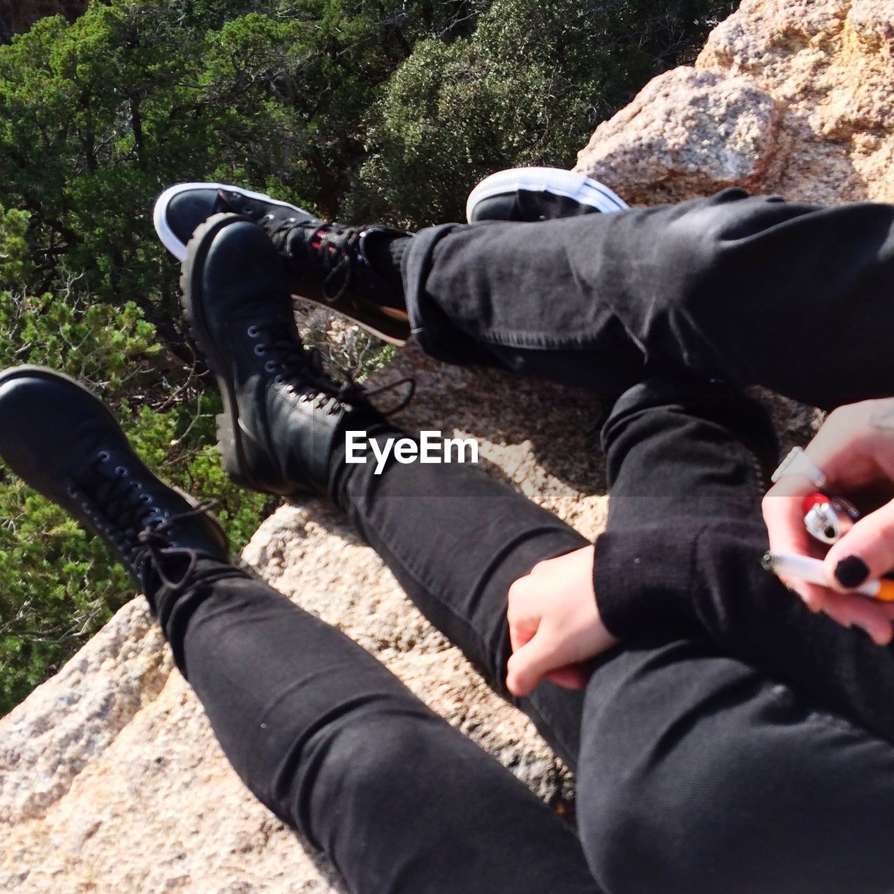 Low section of friends smoking while sitting on rocks