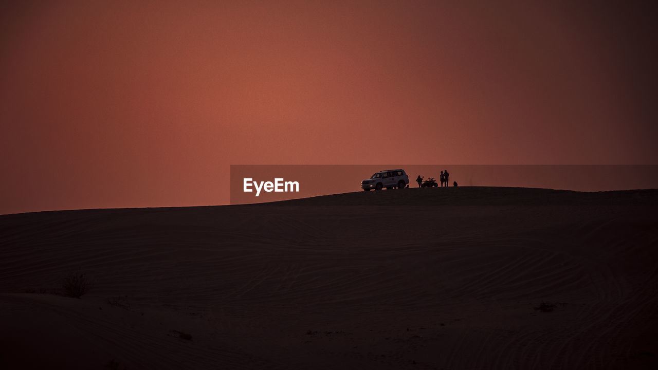 Off-road vehicle at desert against sky during sunset