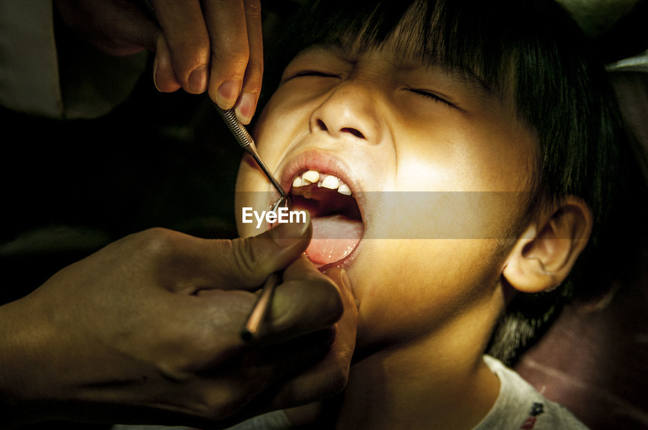 Cropped hand of pediatric dentist examining boy teeth