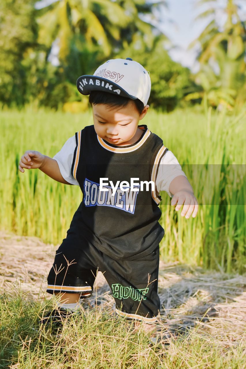 childhood, child, men, one person, plant, nature, grass, agriculture, front view, land, hat, spring, clothing, day, field, toddler, outdoors, cap, person, green, sports, standing, full length, leisure activity, casual clothing, headwear, rural scene, looking, protection, portrait