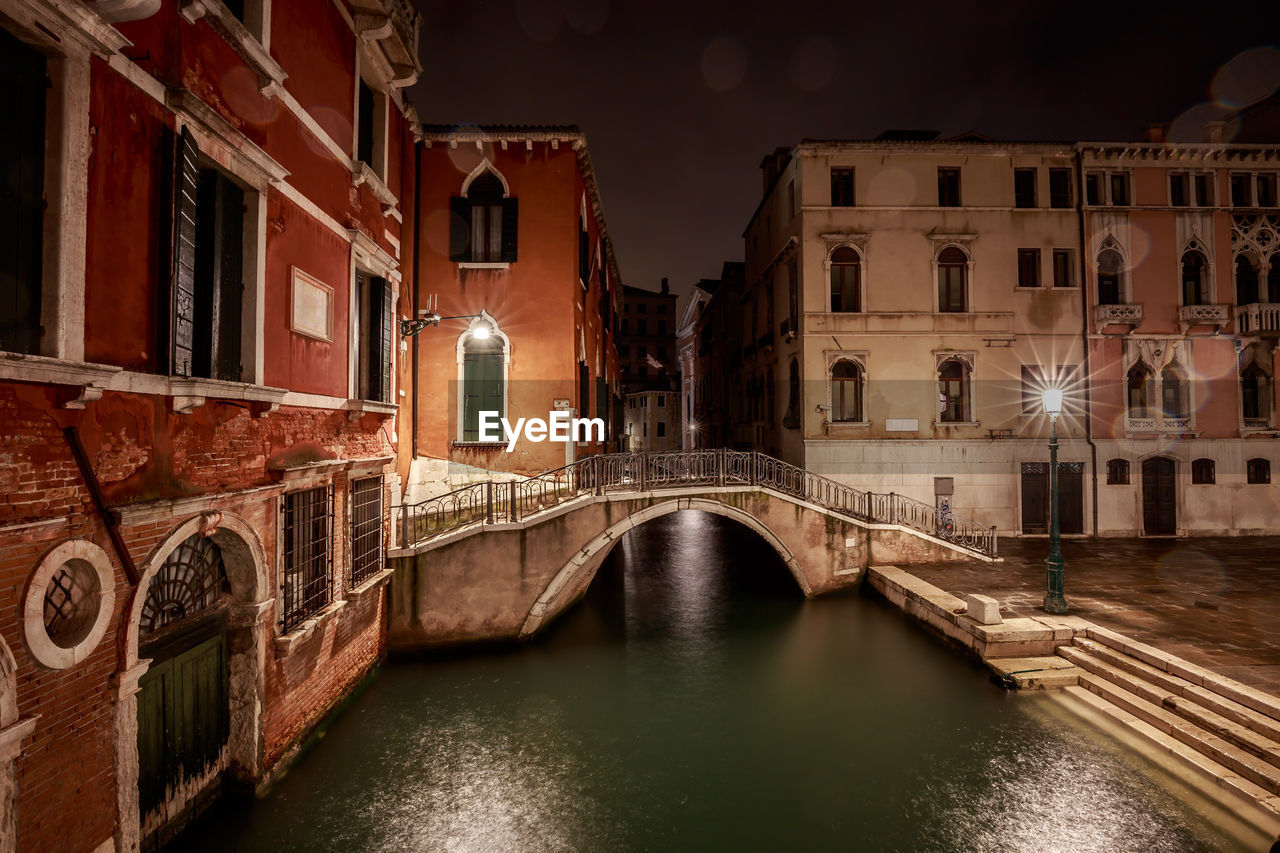 Bridge over canal amidst buildings in city at night