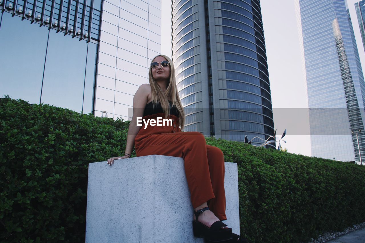 Low angle view of woman sitting against skyscraper