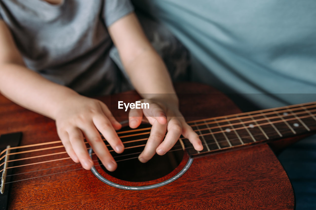 A cute kid plays with a big acoustic guitar at home