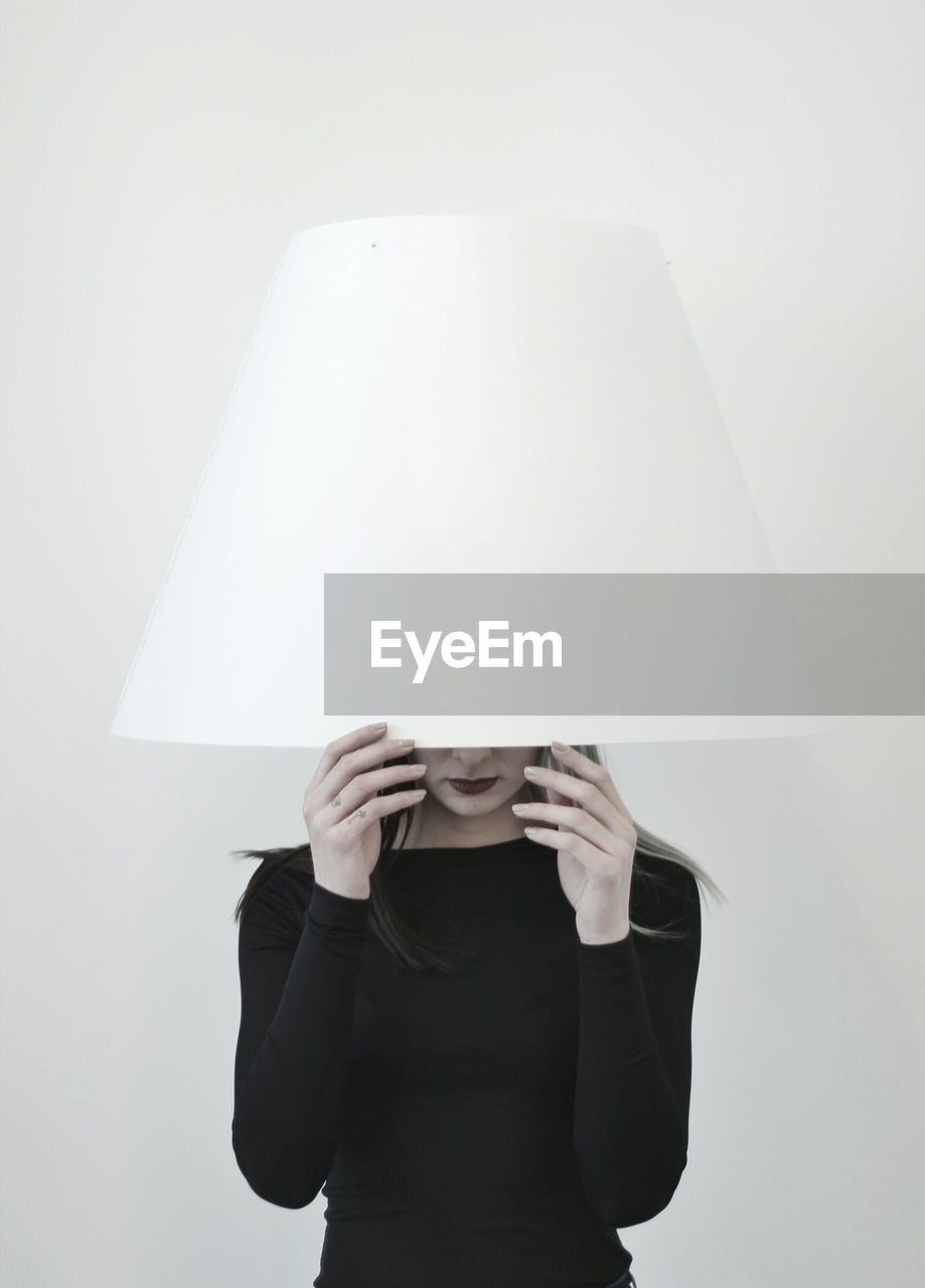 Woman wearing lamp shade while standing against white background