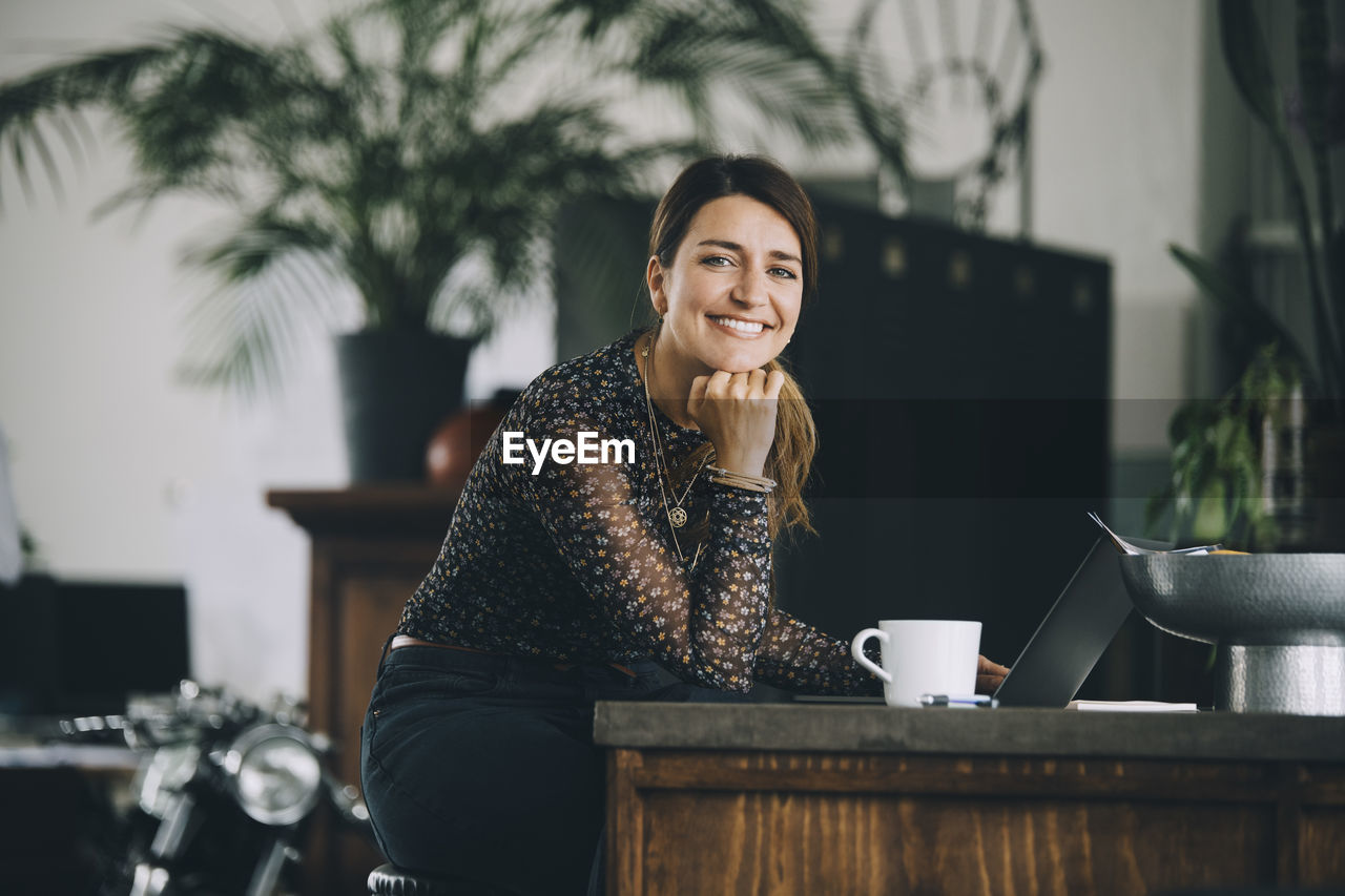 Portrait of smiling businesswoman with hand on chin sitting at kitchen island in creative office