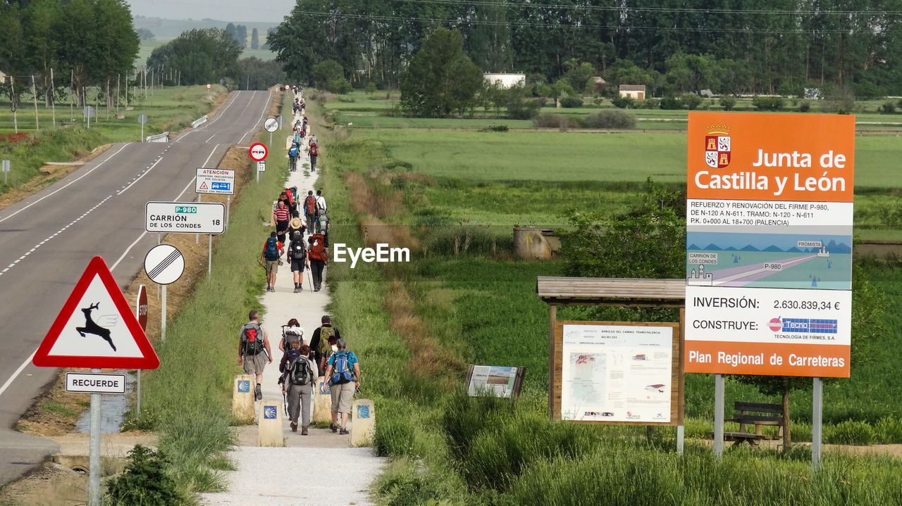 Rear view of people walking on footpath amidst field