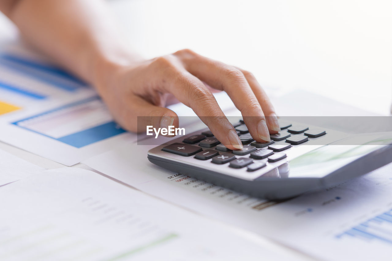 Cropped hand of businesswoman using calculator on desk