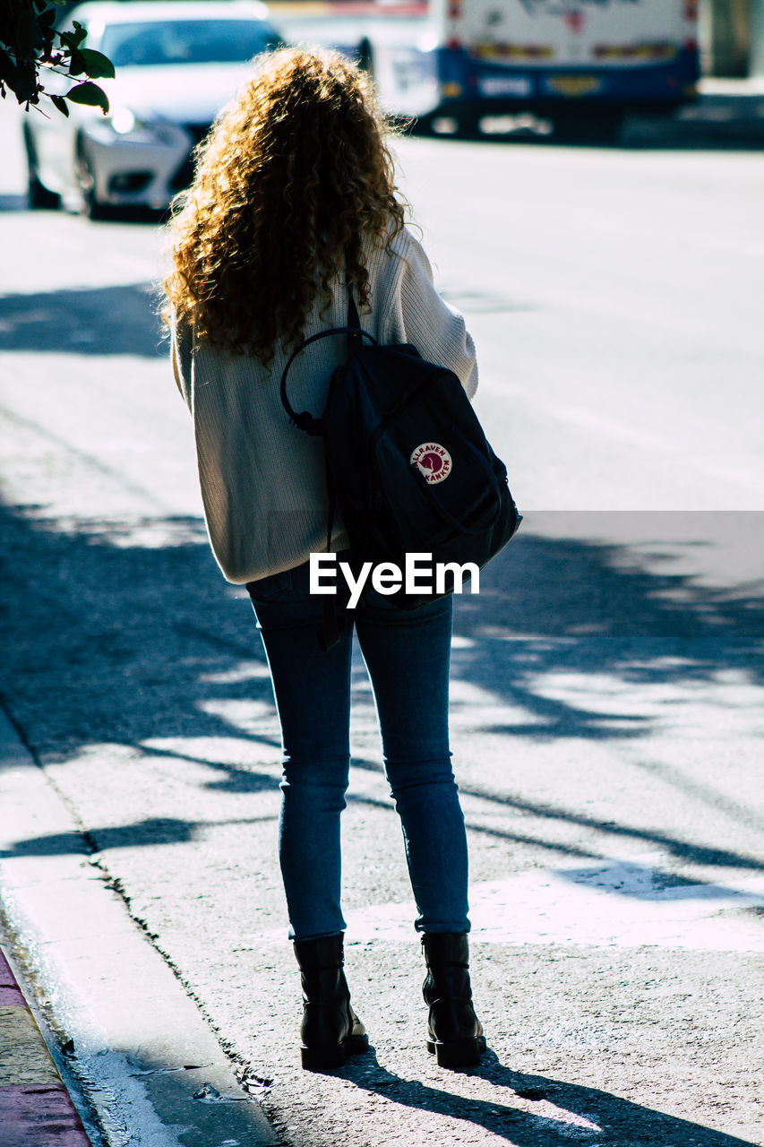 REAR VIEW OF WOMAN STANDING ON FOOTPATH BY STREET