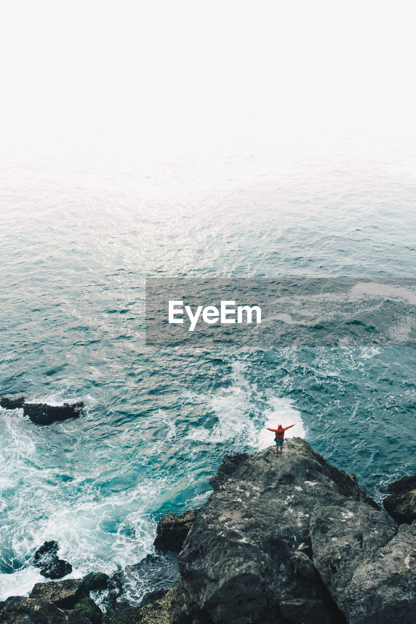 High angle view of woman on cliff by seascape against sky