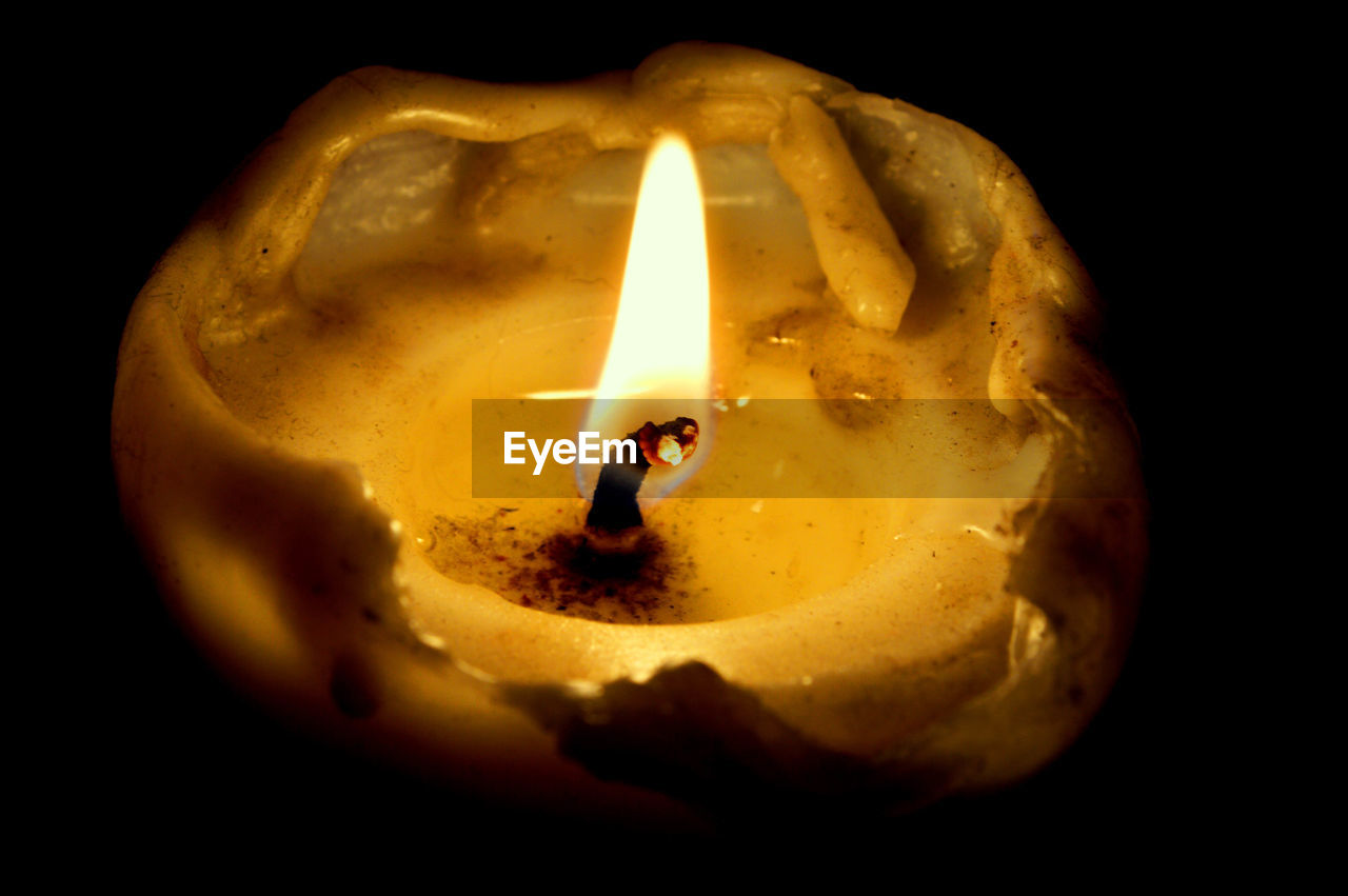 CLOSE-UP OF LIT CANDLE IN DARK