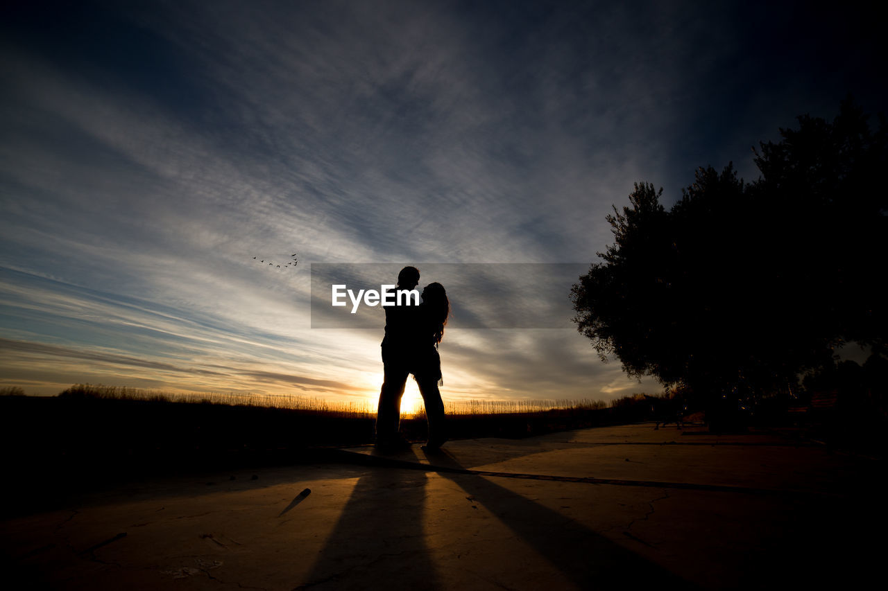 SILHOUETTE OF PEOPLE ON ROAD AT SUNSET