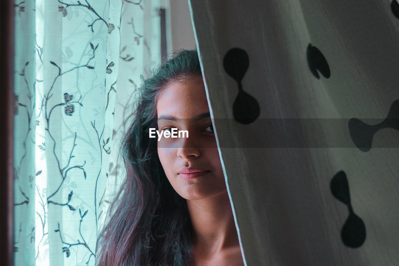 Portrait of teenage girl standing by curtain at home