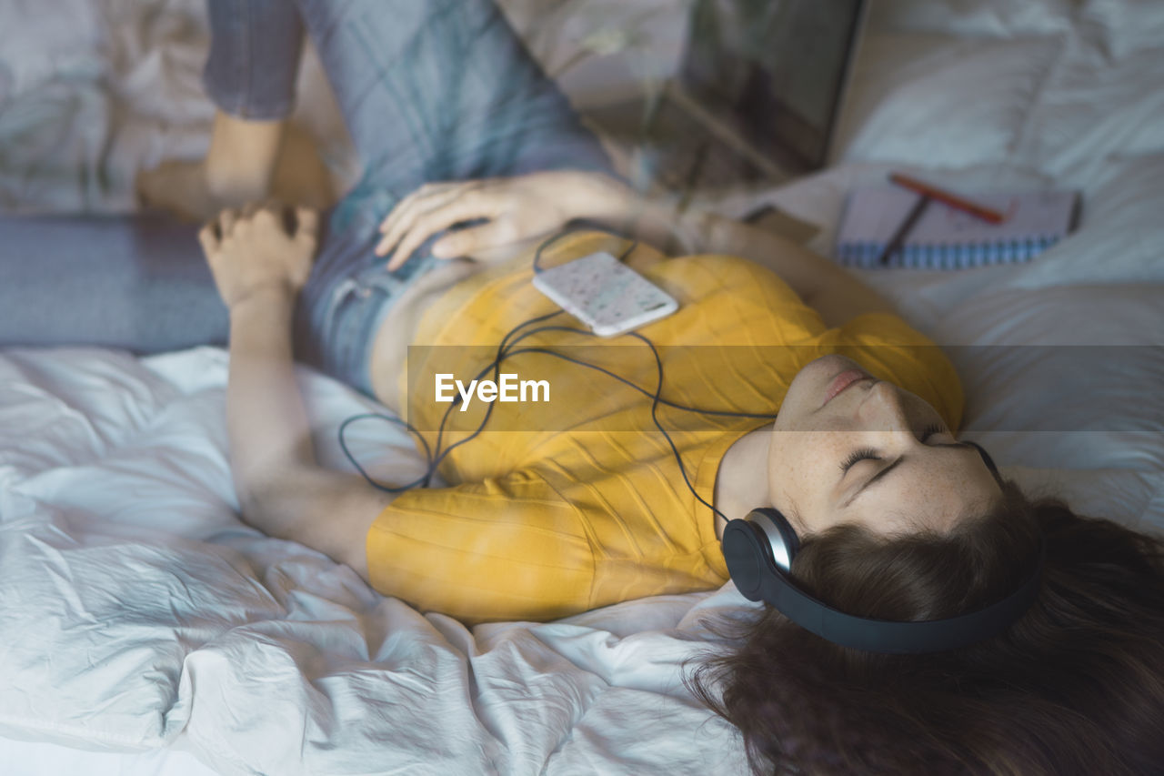 Young woman lying on bed listening music with headphones and smartphone