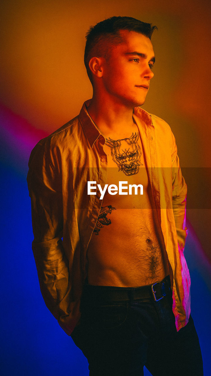 Young man looking away while standing against orange background