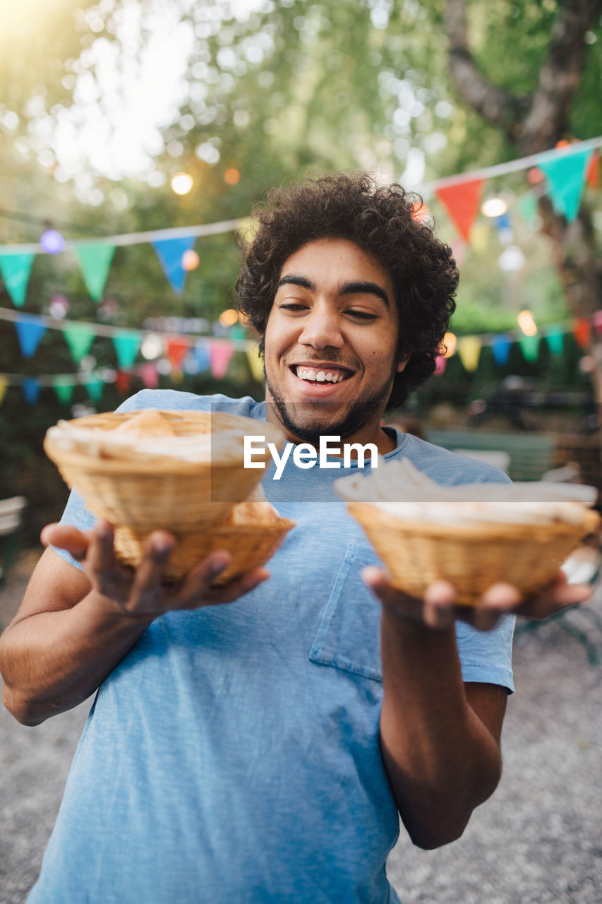 Smiling young man carrying food in bowls during garden party