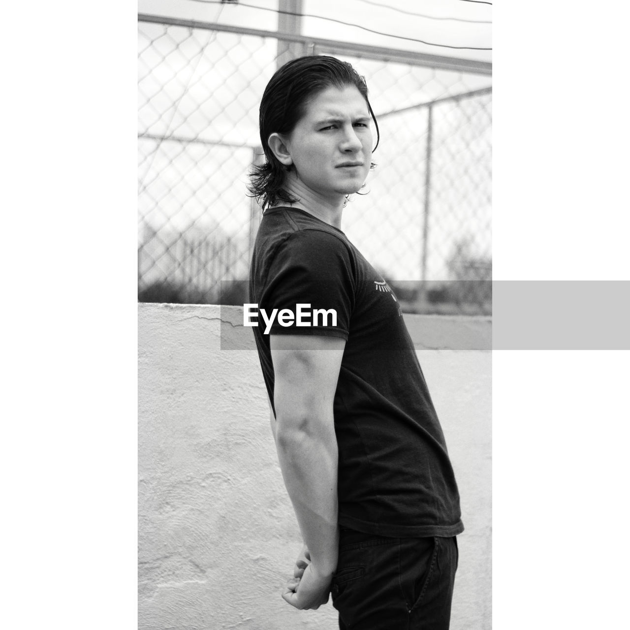 PORTRAIT OF WOMAN LOOKING AWAY WHILE STANDING AGAINST FENCE