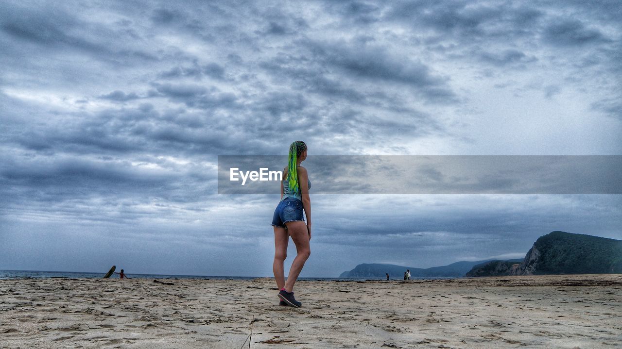 Rear view of woman standing on beach against sky